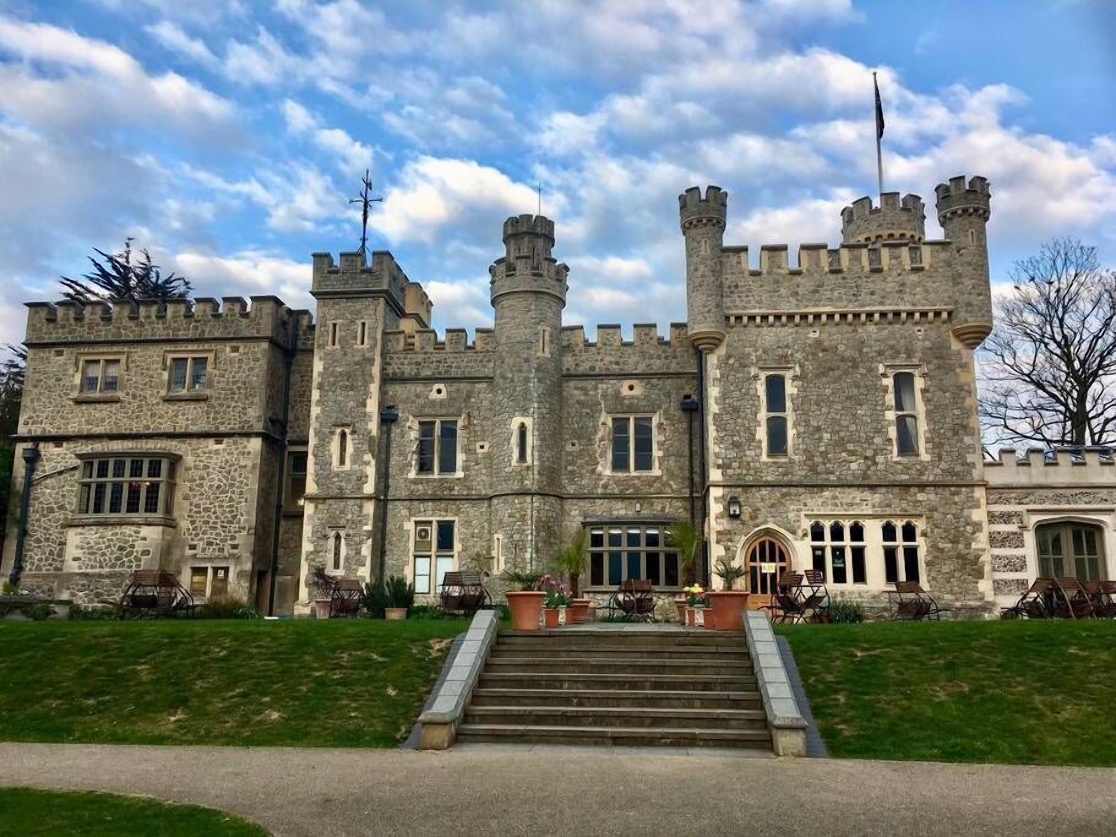 Un edificio de estilo castillo con múltiples torres, una entrada central con escalones y muros de piedra.