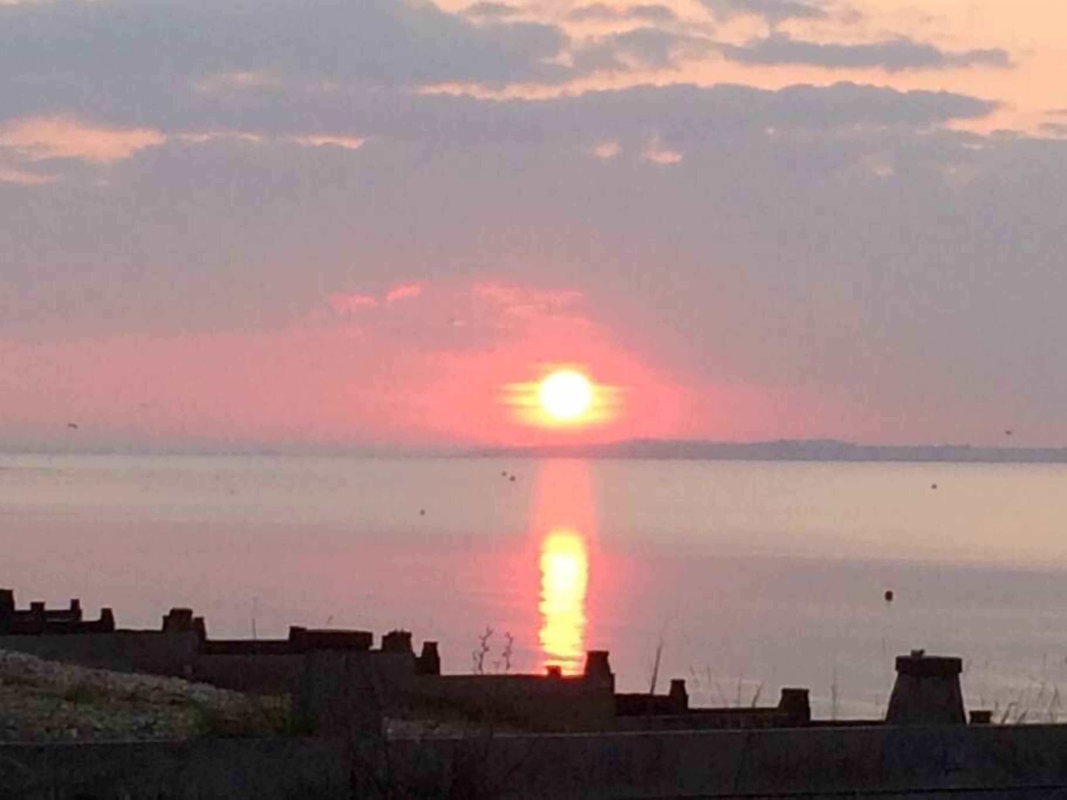 Ein Sonnenuntergang über ruhigem Wasser mit einer fernen Küste.