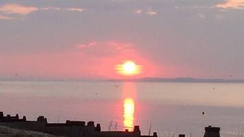 Ein Sonnenuntergang über ruhigem Wasser mit einer fernen Küste.