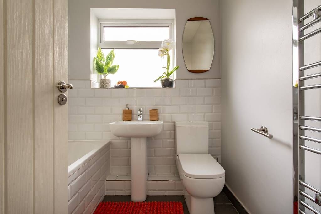 Un baño con lavamanos, inodoro y ventana sobre el lavamanos.