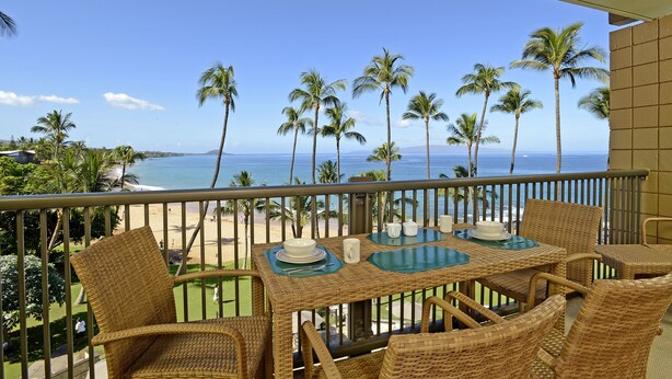 A balcony with wicker furniture, a table set with plates and cups, and a view of the beach and ocean.