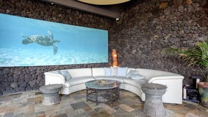 A modern living room with a stone wall, a large flat-screen TV, a white sectional sofa, a round coffee table, and two stone planters.