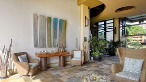 A spacious lobby with wicker furniture, a stone coffee table, and large windows offering a view of greenery.