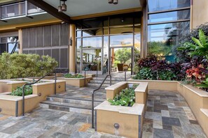A hotel entrance with a stone-tiled patio, outdoor seating, and lush greenery.