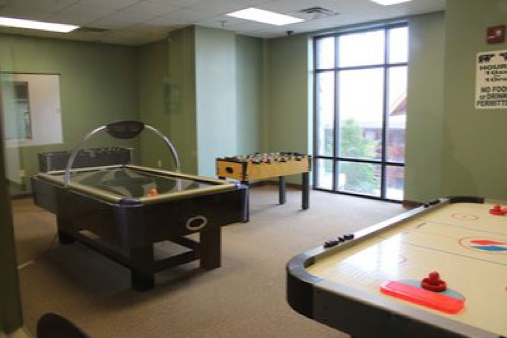 Une table de billard et une table de baby-foot se trouvent dans une pièce aux murs verts et dotée d’une grande fenêtre.