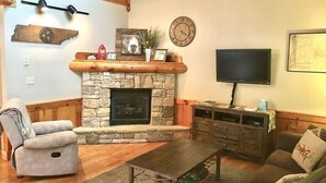 A cozy living room with a stone fireplace, wooden furniture, a mounted television, and a clock on the wall. - Dollywood pigeon forge Cabin, Pools, Game Room, Hot tub, 0.5 mile to Parkway (Pigeon Forge)