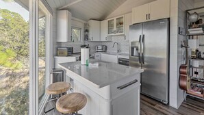 A modern kitchen with white cabinetry, a stainless steel refrigerator, and a large island with stools. - Ocean-View Treetop Escape w/ Fire Pit! (Hilton Head)