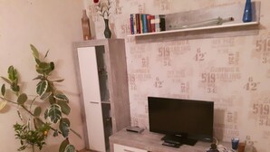 A living room with a TV on a wooden stand, a cabinet, and a potted plant. - Vacation apartment, good location in the mining region Erzgebirge, mountain town Schneeberg (Schneeberg, Sachsen, Deutschland)