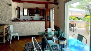 A kitchen with wooden cabinets, a hanging flower arrangement, and a dining area with a glass table and chairs. - Air-conditioned "Carmen" villa with heated pool near the ocean (Biscarrosse)