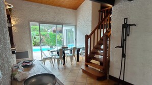 A modern kitchen with a wooden staircase, a dining area with a glass table, and a view of a swimming pool. - Air-conditioned "Carmen" villa with heated pool near the ocean (Biscarrosse)