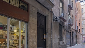 Une rue étroite, avec une librairie sur la gauche, un magasin fermé dont la porte est noire, et un immeuble avec des balcons sur la droite.
