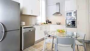 Une cuisine moderne dotée d’appareils électroménagers en acier inoxydable, de meubles blancs et d’une table à manger en verre.