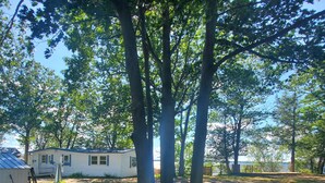 A residential area with a white house, a covered porch, and a fenced yard with trees. - Lake Champlain Waterfront: Amazing Sunsets, Private Beach, and Firepit (Swanton)