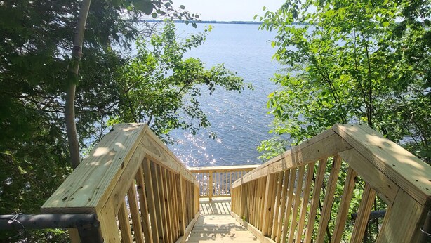 A wooden staircase leading to a viewing platform overlooking a body of water, surrounded by trees. - Lake Champlain Waterfront: Amazing Sunsets, Private Beach, and Firepit (Swanton)