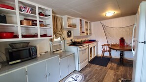 A compact kitchen with white cabinets, a microwave, a stove, and a small dining table with chairs. - Lake Champlain Waterfront: Amazing Sunsets, Private Beach, and Firepit (Swanton)