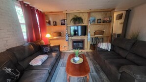 A living room with two leather sofas, a wooden coffee table, a TV, and a fireplace. - Lake Champlain Waterfront: Amazing Sunsets, Private Beach, and Firepit (Swanton)