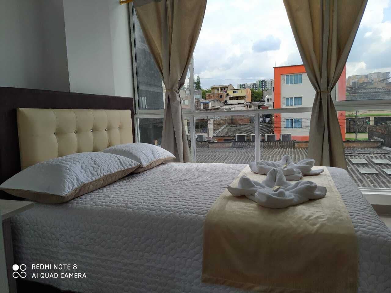 A hotel room with a bed, curtains, and a view of buildings through the window.