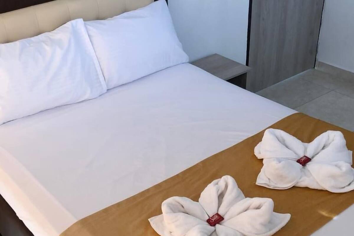 A neatly made bed with white linens and a brown bedspread, featuring two towels arranged in a bow shape with a red tag.