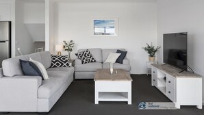 A modern living room with a grey sofa, a coffee table, a TV, and a ceiling fan. - Seacombe Grove, Ventnor with open fire, balcony stunning ocean views (Ventnor)