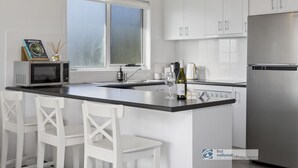 A modern kitchen with white cabinetry, a stainless steel refrigerator, a microwave, and a large window. - Seacombe Grove, Ventnor with open fire, balcony stunning ocean views (Ventnor)