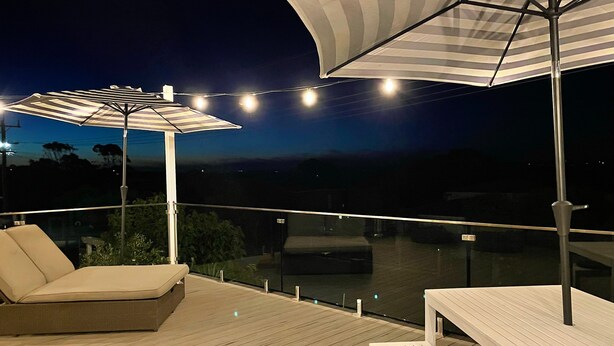 A deck with a sofa, a table, and two umbrellas. - Seacombe Grove, Ventnor with open fire, balcony stunning ocean views (Ventnor)