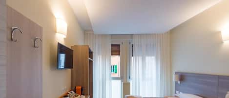 Habitación de hotel con cama, escritorio, silla, televisor y ventana con cortinas.