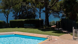 Ein Swimmingpool mit Blick auf das Meer, umgeben von Bäumen und einem Zaun.