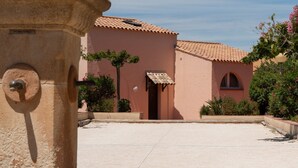 Ein Innenhof mit einer großen Steinfontäne, ein Gebäude mit einem Ziegeldach und einem strahlend blauen Himmel.
