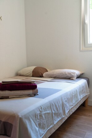 A single bed with a white and brown pillow, a folded blanket, and a wooden floor.
