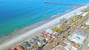 Vista aérea de una zona costera con playa, muelle y aparcamiento con edificios.