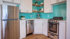 A modern kitchen with white cabinets, a stainless steel refrigerator, a dishwasher, a stove, and a tiled backsplash.