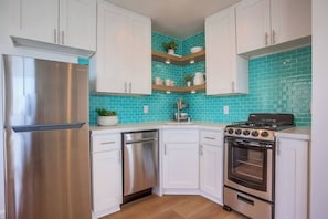 A modern kitchen with white cabinets, a stainless steel refrigerator, a dishwasher, a stove, and a tiled backsplash. - Pacific House #1 - Extreme Oceanfront (Oceanside)