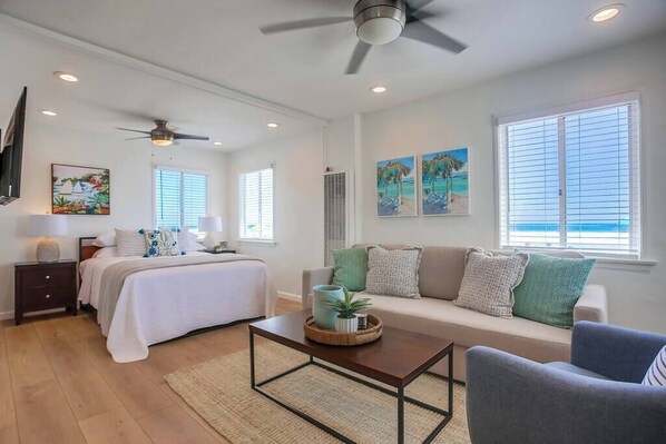 A spacious living room with a bed, a sofa, a coffee table, and artwork on the walls.