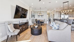 Un salón amplio con televisor grande, comedor y cocina al fondo.