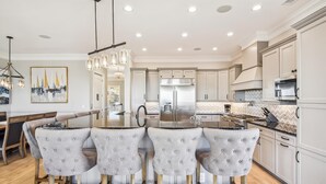 Una cocina moderna con una isla central, electrodomésticos de acero inoxidable y una zona de comedor con una mesa de vidrio y sillas capitonadas.