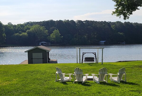 A lakeside setting with a gazebo, Adirondack chairs, and a small shed.