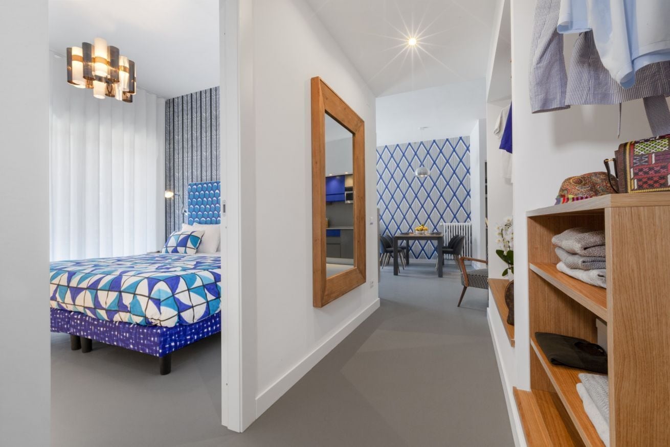Un dormitorio moderno con cama, espejo, armario y zona de comedor con mesa y sillas.