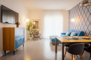 Ein modernes Wohnzimmer mit einem blauen Sofa, einem Holzesstisch und einem an der Wand montierten Fernseher.