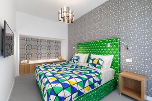 Ein modernes Schlafzimmer mit einem Kopfende mit geometrischem Muster, einer farbenfrohen geometrischen Bettdecke und einer grünen, gepolsterten Bank.