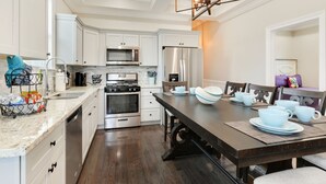 Una cocina moderna con armarios blancos, electrodomésticos de acero inoxidable y una mesa de comedor de madera para cuatro personas.