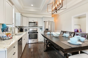 A modern kitchen with white cabinetry, stainless steel appliances, and a wooden dining table set for four. - Creole Queen with Pool, 5 bedrooms with off-street parking (New Orleans)