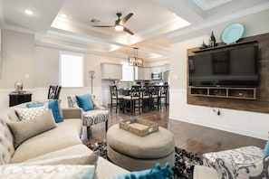 A spacious living room with a large flat-screen TV mounted on the wall, a ceiling fan, and a dining area in the background. - Creole Queen with Pool, 5 bedrooms with off-street parking (New Orleans)
