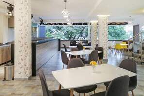 A modern dining area with tables and chairs, a view of trees outside, and a staircase leading to an upper level.