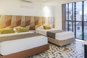 A hotel room with two beds, a patterned headboard, a large window, and a terrazzo floor.