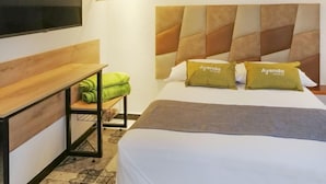 Hotelkamer met een bed, een aan de muur bevestigde televisie, een houten bankje en een klein tafeltje met een handdoek.