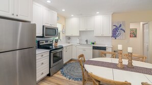 A modern kitchen with white cabinets, stainless steel appliances, a microwave, and a dining area with a round table and chairs. - Sizzling Prices-COOL Summer Retreat (Cocoa Beach)