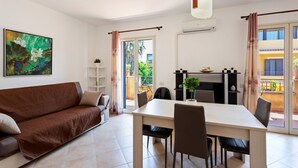 En moderne stue med sofa, spisebord, stole, en hængende lampe, et maleri og en balkon med udsigt.