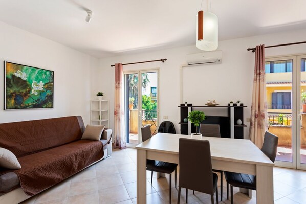 Ein modernes Wohnzimmer mit einer Couch, einem Esstisch, Stühlen, einer Hängeleuchte, einem Gemälde und einem Balkon mit Blick.