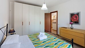 Et soveværelse med en seng, et garderobeskab, en kommode, en lampe og et billede i ramme på væggen.