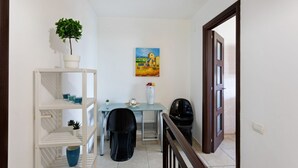 Une pièce comprenant une table à manger, des chaises, une plante en pot, un tableau accroché au mur et une porte donnant sur une autre pièce.